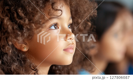 Close up of a young girl with curly hair, listening intently during a school lesson, radiating curiosity and engagement while embracing her educational journey 127806087