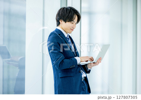 オフィスでノートパソコンを持つ若いビジネスマン オフィスでノートパソコンを持つ若いビジネスマン 127807305