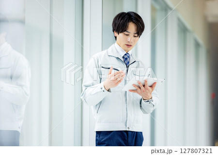 オフィスの廊下でタブレットを操作する作業着の男性 オフィスの廊下でタブレットを操作する作業着の男性 127807321