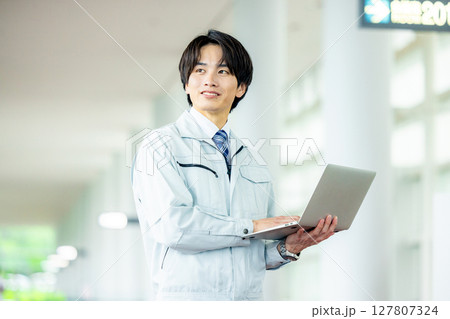 オフィスの廊下でノートパソコンを持つ作業服の若い作業員 オフィスの廊下でノートパソコンを持つ作業服の若い作業員 127807324