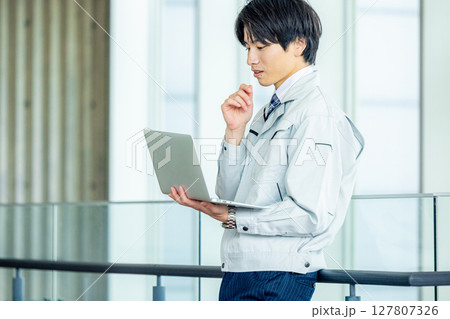 オフィスの廊下でノートパソコンを持つ作業服の若い作業員 オフィスの廊下でノートパソコンを持つ作業服の若い作業員 127807326