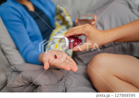Caring Gesture Giving Medication with Water on a Cozy Couch, Creating Comfort 127808595