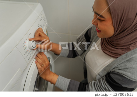 A woman skillfully adjusting the laundry settings on her washing machine at home 127808613