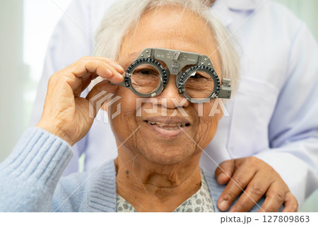 Optometrist checking Asian elderly woman ophthalmic vision eye test and using optical trial frame. 127809863