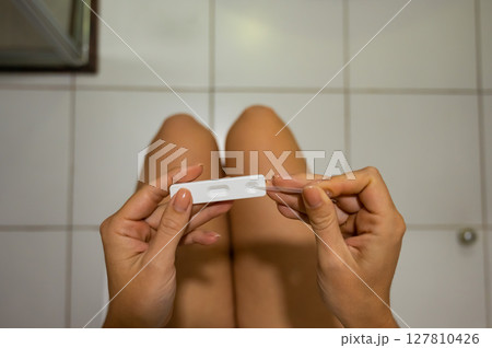 A woman takes an express pregnancy test while sitting on the toilet. A woman takes an express pregnancy test while sitting on the toilet. 127810426