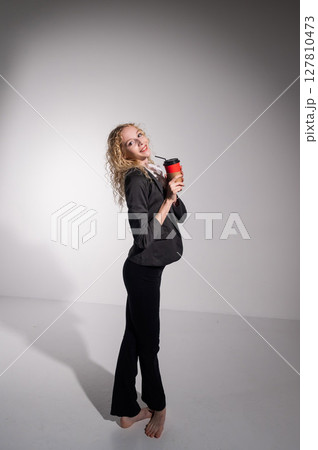 Barefoot ballerina in business suit dancing with a cup of coffee on a white background.  127810473