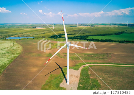 A row of large wind turbines stands tall in a vast, open field, showcasing renewable energy production. A row of large wind turbines stands tall in a vast, open field, showcasing renewable energy production. 127810483