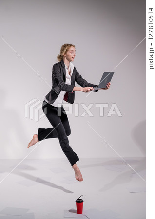 Barefoot ballerina in business suit jumping with laptop on white background. Barefoot ballerina in business suit jumping with laptop on white background. 127810514