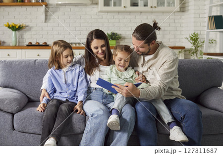 Young happy family reading a book with cute daughter and son sitting on sofa at home Young happy family reading a book with cute daughter and son sitting on sofa at home 127811687