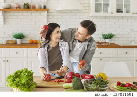 Happy healthy funny couple amuse cooking salad in modern kitchen, playing holding fresh vegetables 127811691