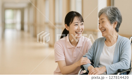 車椅子に座るシニアの日本人女性と若い介護士の女性(16:9横長バナー) 127814420