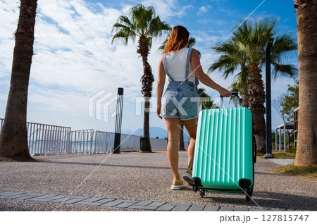 A Caucasian woman walks with a suitcase to the coast. A Caucasian woman walks with a suitcase to the coast. 127815747