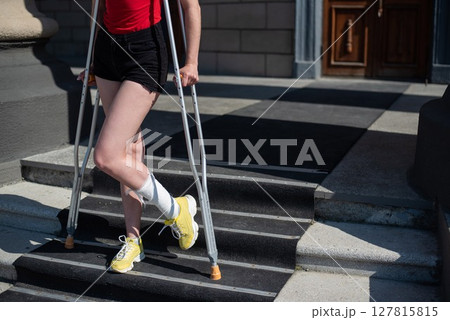 Young red-haired woman in shorts moves with crutches outdoors. Young red-haired woman in shorts moves with crutches outdoors. 127815815