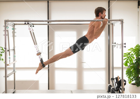 A man performs aerial exercises on a reformer machine. A man performs aerial exercises on a reformer machine. 127818133