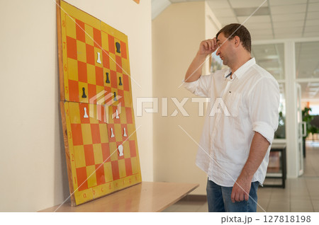 Caucasian man standing at wall mounted magnetic chessboard demonstration.  127818198