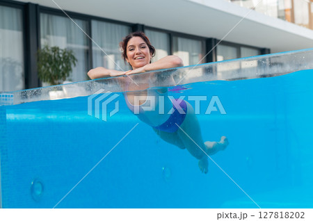 Happy caucasian woman swims in an outdoor pool with a transparent wall in a hotel 127818202