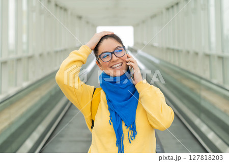 Happy woman stands on a travelator and talks on a cell phone 127818203
