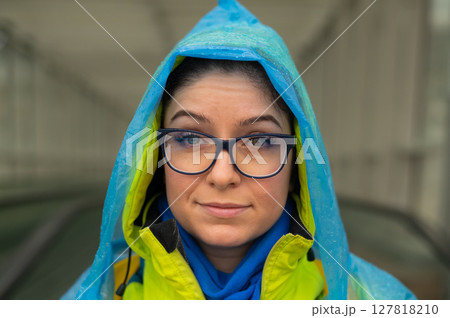Portrait of a smiling woman with glasses wearing a raincoat outdoors. 127818210