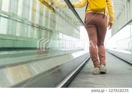 Rear view of a woman with a backpack moving on a travolator 127818235