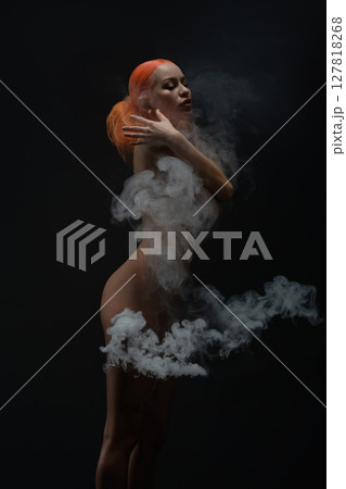 Red-haired woman poses nude with fabric and smoke in serene artistic display Red-haired woman poses nude with fabric and smoke in serene artistic display 127818268