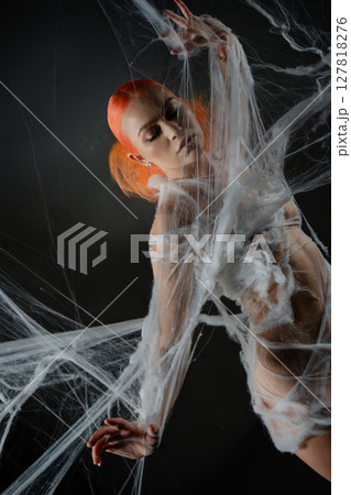 Red-haired woman entangled in an intricate net trap against a dark backdrop Red-haired woman entangled in an intricate net trap against a dark backdrop 127818276