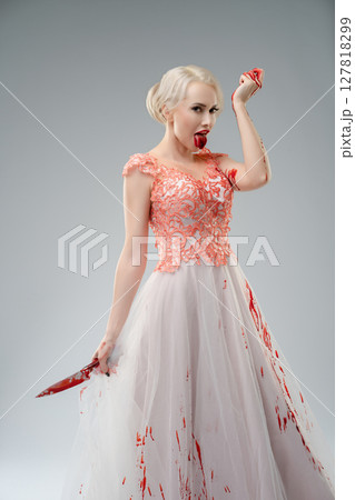 Bride in a blood-soaked dress posing dramatically in a studio setting 127818299