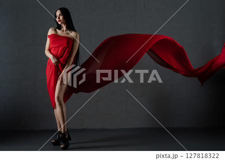 Elegant woman draped in flowing red fabric accentuates beauty and allure 127818322