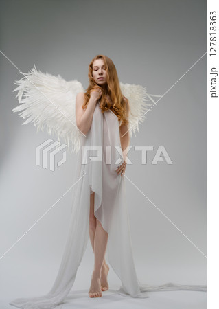Red naked woman poses with angel wings and body art in studio setting 127818363