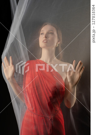 Woman posing gracefully in a red dress with sheer fabric in a dramatic studio setting evoking strong emotion Woman posing gracefully in a red dress with sheer fabric in a dramatic studio setting evoking strong emotion 127818364