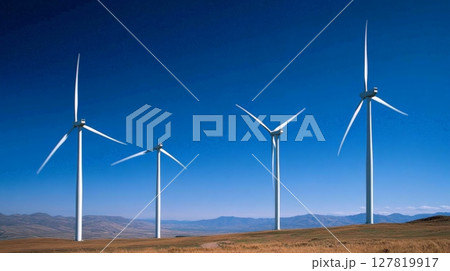 Four wind turbines are actively generating renewable energy on a clear day, contributing to a sustainable future with clean power against a backdrop of distant mountains and blue sky 127819917