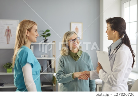 Doctor And Nurse Shaking Hands With Elderly Patient During Hospital Visit 127820726