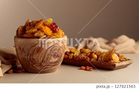 Yellow sultana raisins in a wooden bowl on a beige background. Yellow sultana raisins in a wooden bowl on a beige background. 127821563