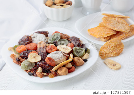 Mix of dried tropical fruits, nuts, and raisins on a white table. 127821597