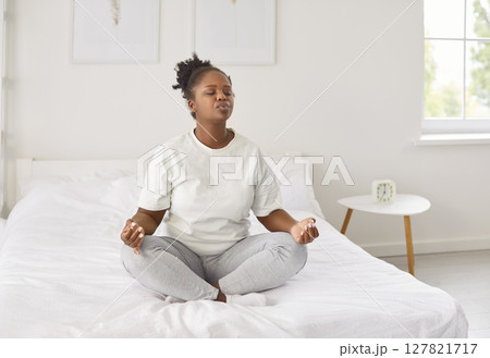 African american woman peaceful on comfortable soft bed, relaxing in lotus pose enjoying practicing  127821717