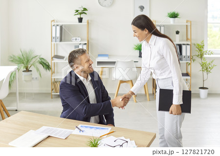 Two business people standing in office making deal shaking hands celebrating business achievement. Two business people standing in office making deal shaking hands celebrating business achievement. 127821720