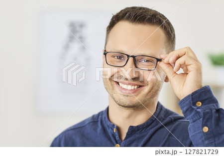 Smiling man choosing and trying on glasses in ophthalmology clinic, optical store to improve vision. Smiling man choosing and trying on glasses in ophthalmology clinic, optical store to improve vision. 127821729
