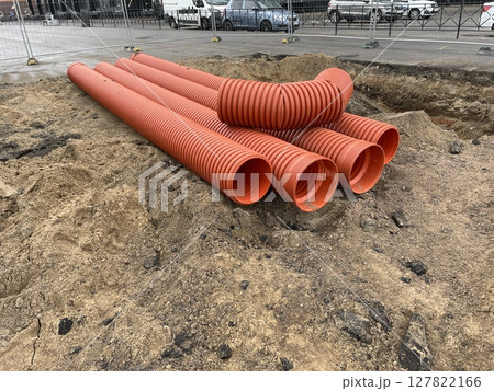 A construction site with bright orange pipes, excavated materials, and equipment 127822166