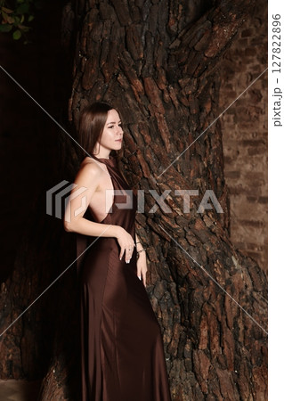 An Elegant Woman Posed Gracefully Against a Beautifully Textured Tree Bark Background 127822896