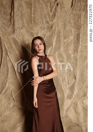 An Elegant Woman Gracefully Posing in a Beautiful Brown Dress Against a Textured Background 127822970