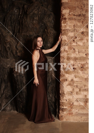 An Elegant Woman in a Beautiful Brown Dress Poses Gracefully Against a Rustic Background An Elegant Woman in a Beautiful Brown Dress Poses Gracefully Against a Rustic Background 127823062