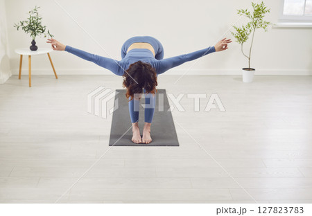 Sporty yogi woman working standing in Uttanasana with palms, hands wide open, head to knees 127823783