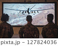 Soldiers in camouflage observe military drone operation on large screen, focusing on aerial surveillance and strategic mission planning 127824036