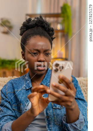 African American sad amazed woman reacts with shock while reading unexpected news on smartphone African American sad amazed woman reacts with shock while reading unexpected news on smartphone 127825179