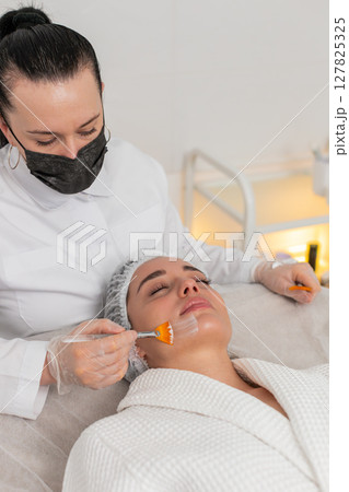 Enzyme therapy, beautician applying moisturizing medical cream on young woman face with brushes 127825325
