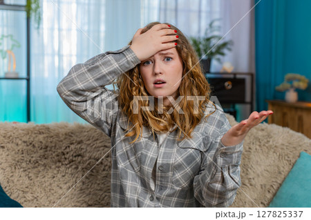 Woman sits on sofa making facepalm gesture feeling disappointed frustrated after unexpected failure Woman sits on sofa making facepalm gesture feeling disappointed frustrated after unexpected failure 127825337