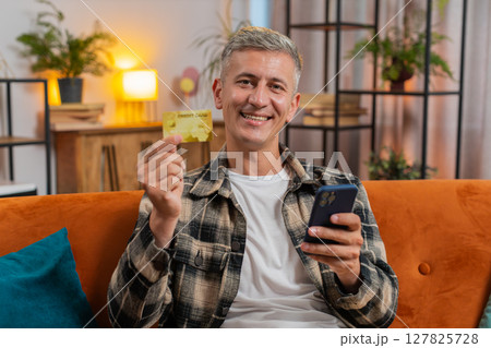 Man using credit bank card and smartphone while transferring money purchases online shopping at home Man using credit bank card and smartphone while transferring money purchases online shopping at home 127825728