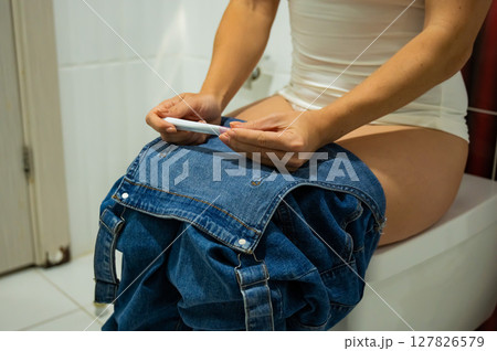 A woman takes an express pregnancy test while sitting on the toilet. A woman takes an express pregnancy test while sitting on the toilet. 127826579