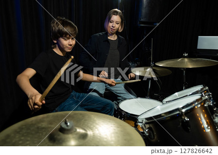 Young caucasian woman teaches a boy to play the drums in the studio on a black background. Music school student 127826642