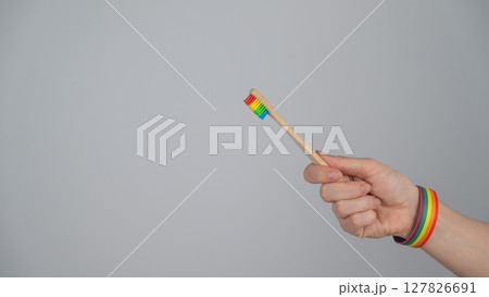 Woman wearing bracelet holds toothbrush with rainbow flag.  127826691
