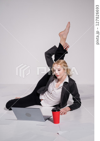 Barefoot ballerina dressed in a business suit poses for a laptop and drinks coffee. Flexible woman works at the computer Barefoot ballerina dressed in a business suit poses for a laptop and drinks coffee. Flexible woman works at the computer 127826693